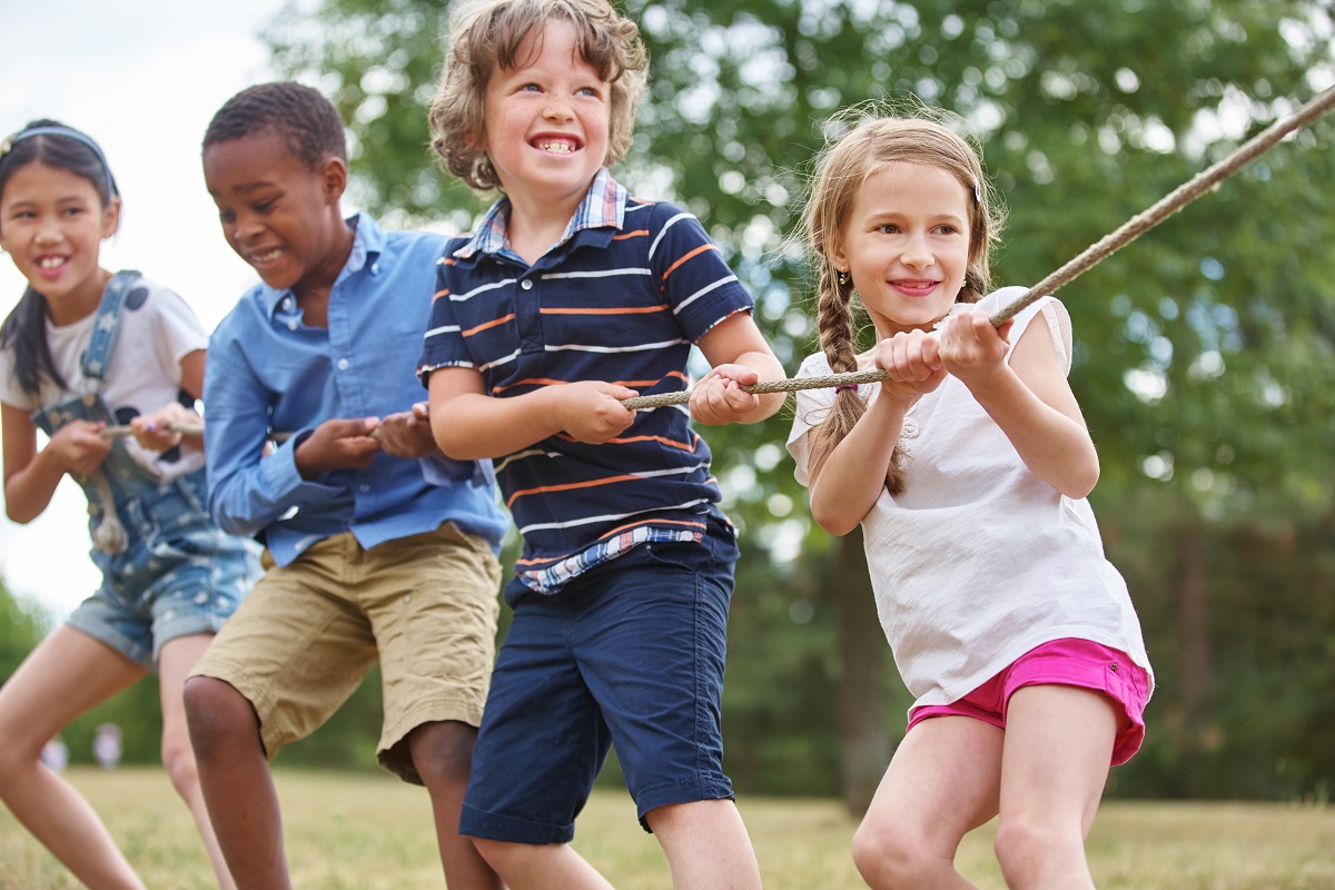 A picture showing four children - three boys and a girl - enjoying a tug of war competition in a grassy park on a summer's day.