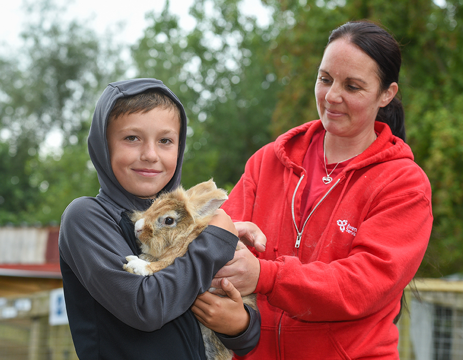 Child holding a rabbit with adult assistance in an outdoor natural setting.